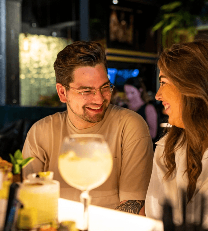 Two people smiling on a date sitting at a bar with a drink